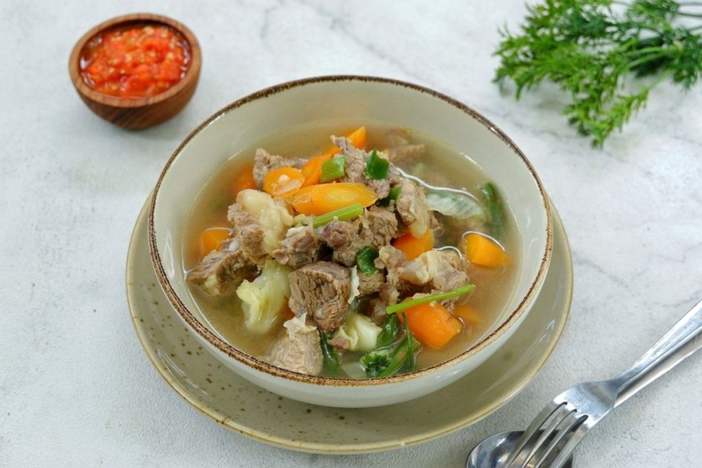 Sup daging gurih berempah dengan kuah bening, wortel, kentang, dan taburan bawang goreng